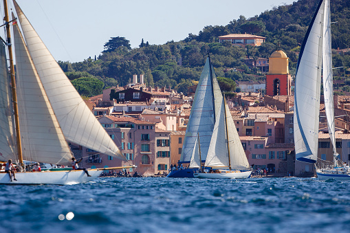 Optimist boats, with Le Lavandou town in background. Four small sailing vessels in single file, navigate behind each other. Le Lavandou, in Var in France. April 16, 2015