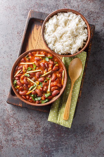 Rajma Masala is a delicious gravy made by cooking red beans with onion, tomatoes and basic spices served with rice close-up on a wooden tray on the table. Vertical top view from above