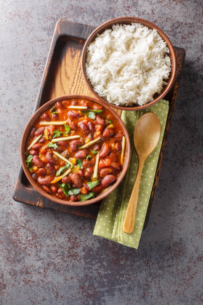 Rajma Masala is a delicious gravy made by cooking red beans with onion, tomatoes and basic spices served with rice close-up on a wooden tray. Vertical top view stock photo