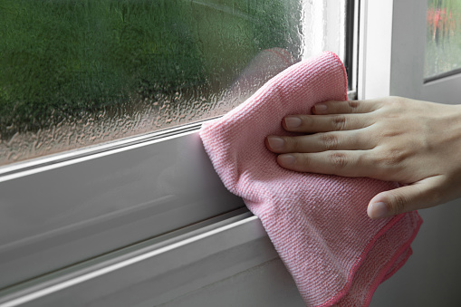 woman wiping window glass with drops of condensate indoor