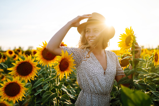 Beautiful woman posing in a field of sunflowers in a dress and hat. Fashion, lifestyle, travel and vacations concept.