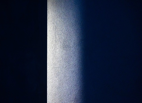An interior shot of a room featuring a tall wall in blue tones in a dark room