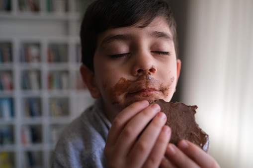Smiling little boy licking messy chocolate from his face