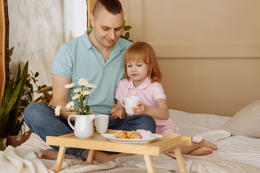 Father and daughter having breakfast in bed in the morning. High quality photo