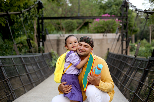 Father hugging with his cute baby daughter after school on the suspension bridge in public park.