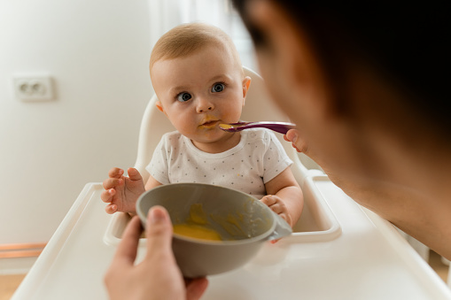 Mother feeding her baby in a high chair with baby food