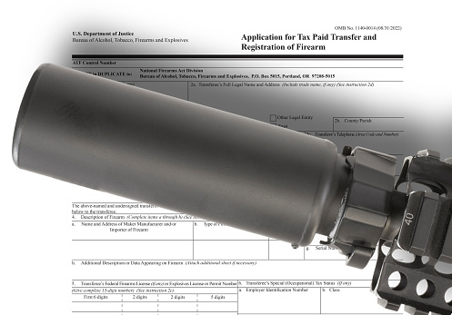 Public domain ATF form to own a suppressor in the background with silencer above
