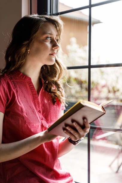 istock Young woman sitting by the window, enjoying reading a book 1497395526
