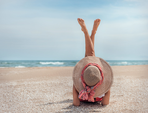 a girl with a hat lying on the beach in front of a beautiful Mediterranean blue sea, with her legs raised.concept summer and vacations.