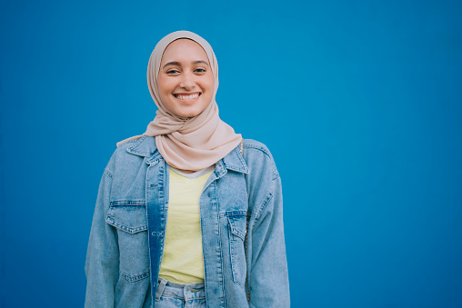 portrait Asian Malay woman with hijab looking at camera smiling standing in front of blue wall