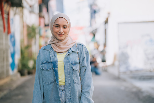 portrait Asian Malay woman with hijab looking at camera smiling standing in city street alley