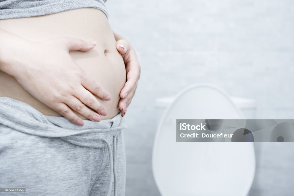 Chronic Constipation with a woman who can't pass stools regularly hand holding big abdominal Chronic Constipation with a woman who can't pass stools regularly hand holding abdominal in a toilet Irritable Bowel Syndrome Stock Photo