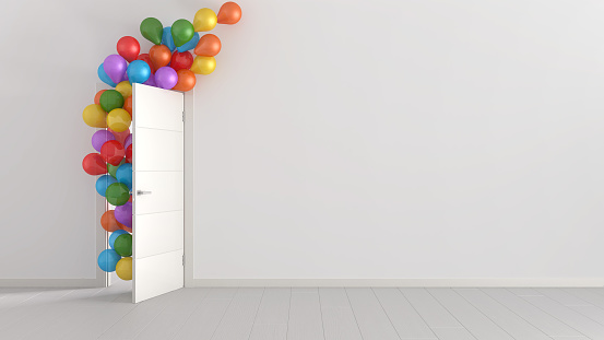 Colorful balloons floating through open door in home interior with white walls and parquet. Template with copy space. Surprise holiday concept