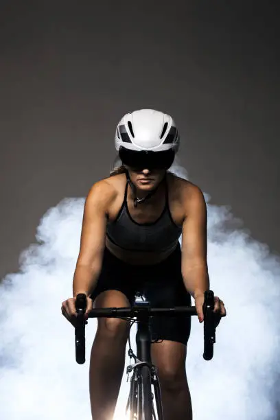 Girl posing on roadbike. White protective helmet and black goggles. Cyclist against foggy background.