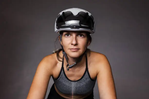 Portrait of a girl on roadbike. White protective helmet and black goggles. Cyclist on foggy background.