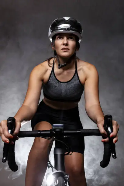 Girl posing on roadbike. White protective helmet and black goggles. Cyclist against foggy background.