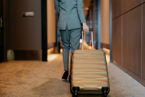 Rear view of an Asian Chinese businesswoman with suitcase walking through hotel corridor