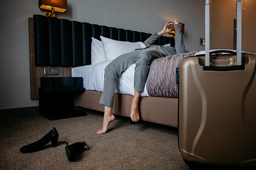 Asian Chinese businesswoman lying on bed resting and using smartphone after checked in hotel room. Business travel concept.