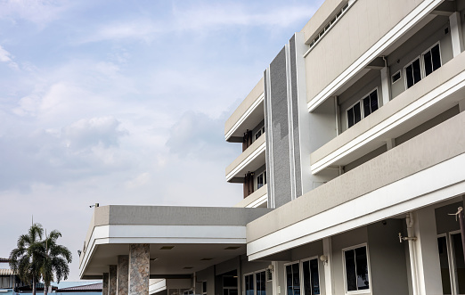 Low angle view of a large brown facade of a hospital with sky clouds in the background during daytime in rural Thailand.