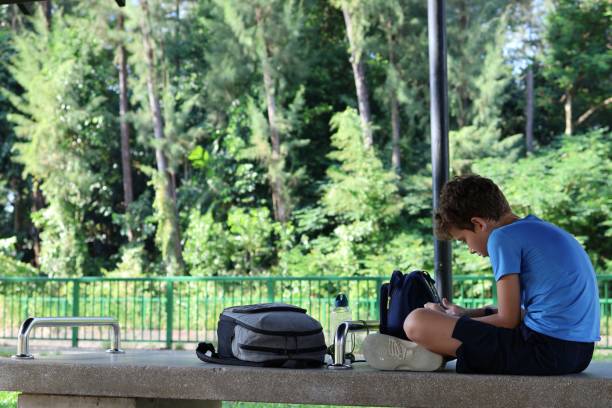 istock elementary school boy sitting with a smartphone in his hands in a green park 1497418689