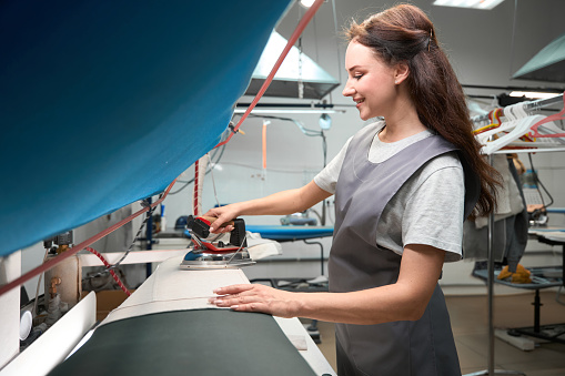 Skilled woman dry cleaner service worker ironing cloth after pressing on steam board, post treatment
