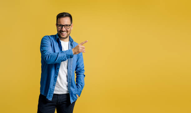 istock Smiling male entrepreneur pointing at copy space for marketing while standing on yellow background 1497421075