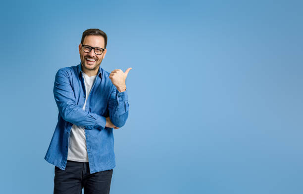 Portrait of cheerful businessman pointing at copy space for advertising against blue background Portrait of cheerful businessman pointing at copy space for advertising against blue background spokesmodel stock pictures, royalty-free photos & images