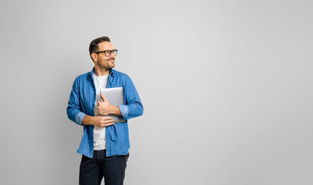 istock Smiling male professional holding digital tablet looking away thoughtfully against white background 1497421115
