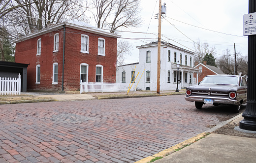 A cobblestone street with historic buildings and a classic car in Belleville, Illinois