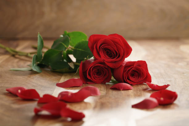 istock three red roses and petals on old wood table with copy space 1497430297