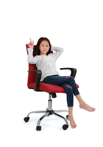 Asian little girl child pointing up and look at camera with sitting and relax on chair isolated on white studio background. Image full length with Clipping path