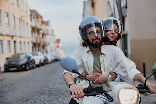 Happy couple in protective hats are riding on vintage scooter in Lisbon street. High quality photo
