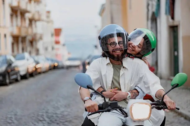 Happy couple in protective hats are riding on vintage scooter in Lisbon street. High quality photo