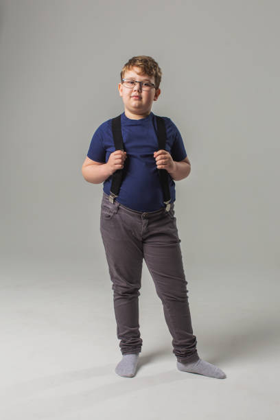 blonder junge in brille und jeans mit hosenträgern im studio auf weißem hintergrund. kindheit. kindheit. schüler - teen obesity stock-fotos und bilder