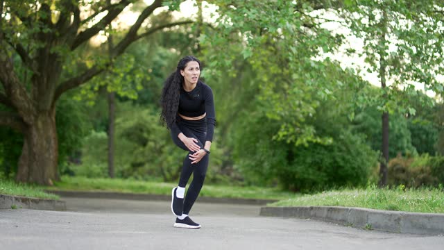 Young woman suffers from painful severe knee joint ache during a morning run in urban city park.
