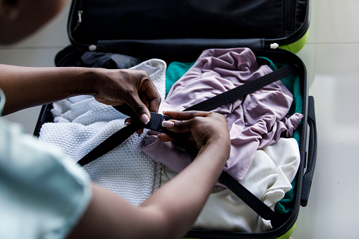 Over the shoulder view of unrecognizable young woman closing clasps in her suitcase after she finished packing for a vacation.