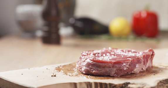 salt falling on raw rib eye steak on board, wide photo