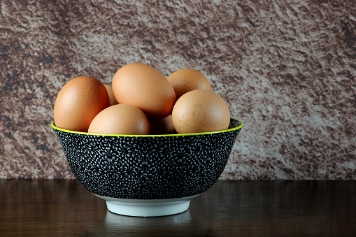 Group of fresh or boiled eggs in a white bowl standing on cloth, square. Studio shot