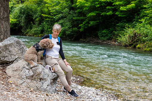 A woman with her dog is sitting and relaxing by the river.