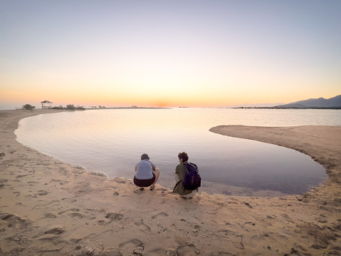 Young multiracial couple beachcombing on an empty sandy island at sunrise.  Pemuteran, Bali, Indonesian.