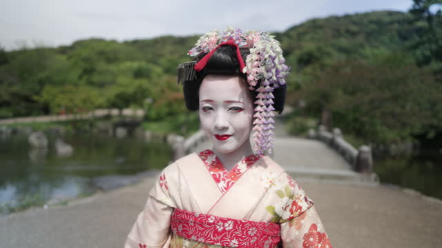 Japanese Maiko (Geisha in training) standing in public park in Gion, Kyoto - holding Japanese traditional paper umbrella
