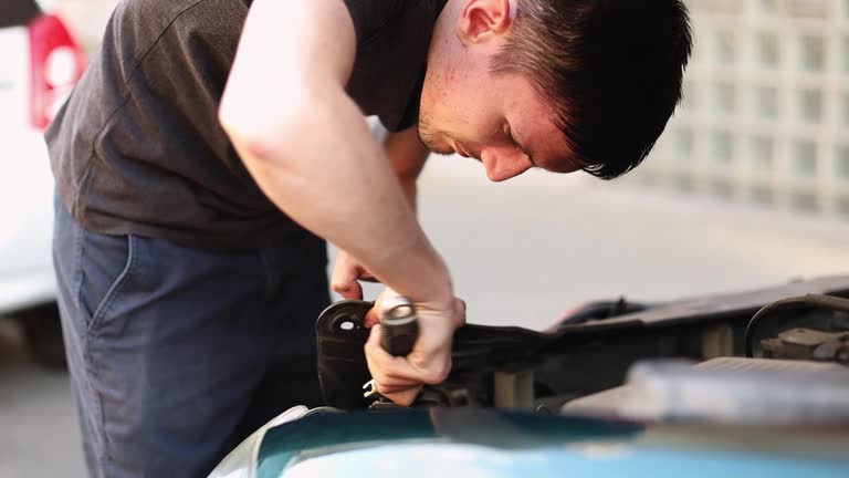 A young guy unwinds a nut with a wrench in the hood of a car.