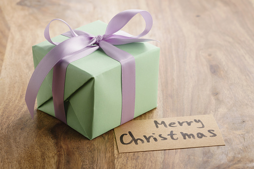 green paper gift box with purple ribbon bow and merry christmas greeting card on old wood table, shallow focus