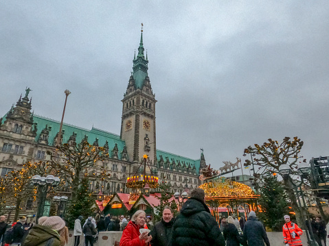 German Christmas market on Hamburg main square on December 4, 2022. Fairy lights and the town hall building by dusk