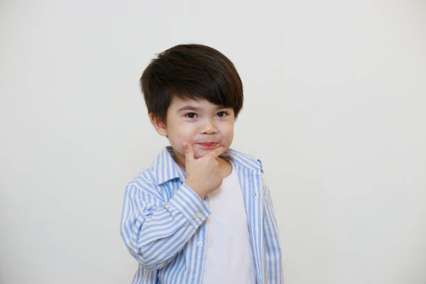 A little boy wearing a polite shirt is thinking using his hands to express emotions against a white background.