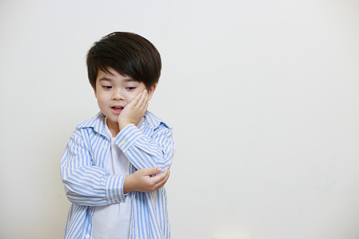 A small boy in a polite shirt poses with his hands to his face and elbows against a white background.