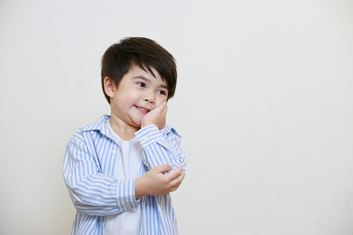 A small boy in a polite shirt poses with his hands to his face and elbows against a white background.