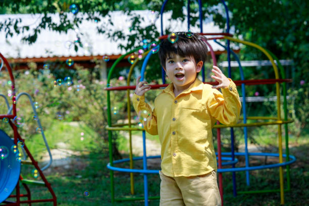 uroczy chłopiec radośnie goniący bańki mydlane w powietrzu na podwórku. - child asian and indian ethnicities facial expression asia zdjęcia i obrazy z banku zdjęć