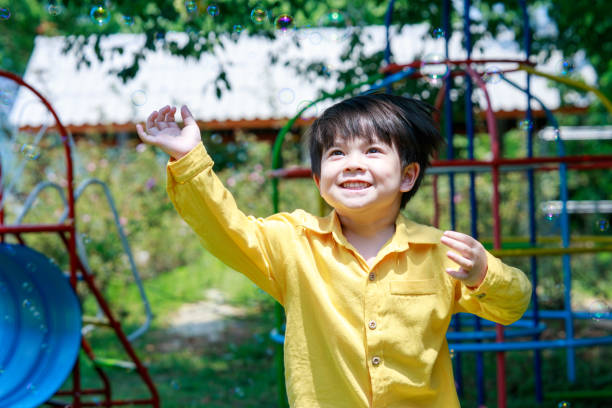 uroczy chłopiec radośnie goniący bańki mydlane w powietrzu na podwórku. - child asian and indian ethnicities facial expression asia zdjęcia i obrazy z banku zdjęć