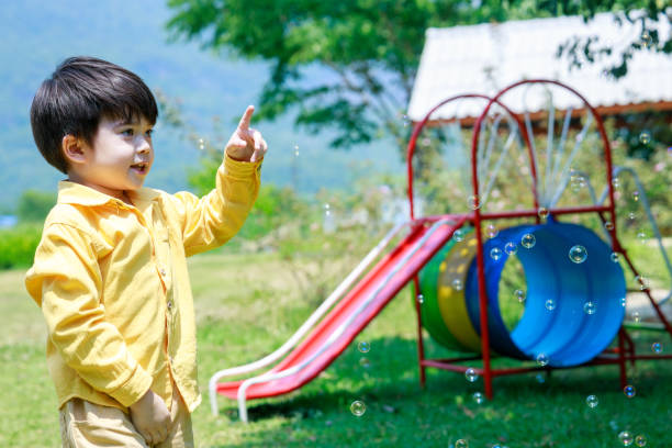 uroczy chłopiec radośnie goniący bańki mydlane w powietrzu na podwórku. - child asian and indian ethnicities facial expression asia zdjęcia i obrazy z banku zdjęć